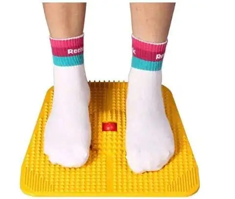 Yellow acupressure foot massager mat with raised nodes, feet resting on top